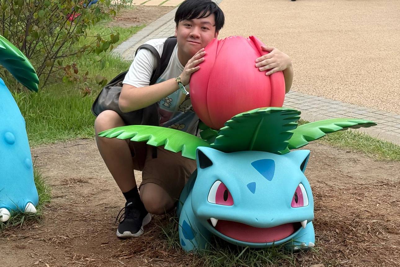 Lucius crouched beside a life-size Ivysaur statue, arms around its flower bulb